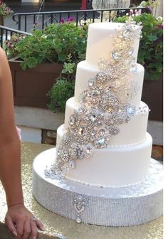 a woman cutting into a white wedding cake with silver decorations on it and flowers in the background