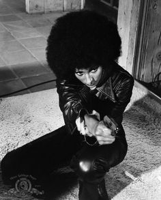 a black and white photo of a man with an afro sitting on the ground looking at his cell phone