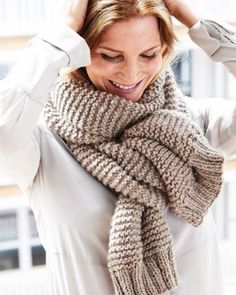 a woman wearing a knitted scarf and holding her hands on her head while looking at the camera