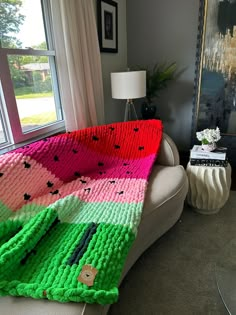 a living room with a couch covered in a knitted watermelon blanket next to a window