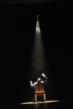 a person sitting on a chair in the dark with their arms up and hands raised