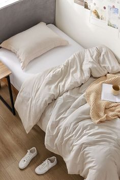 an unmade bed in a bedroom with white shoes on the floor next to it