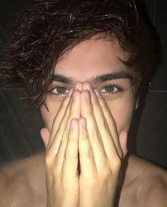 a young man covers his face with his hands as he looks into the camera while standing in front of a mirror