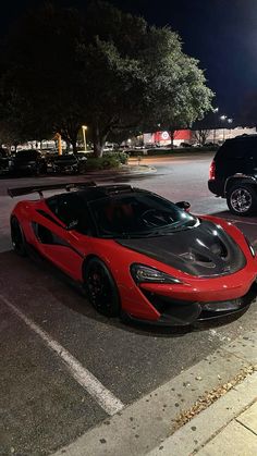 a red and black sports car parked in a parking lot next to other cars at night