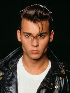 a man in a black leather jacket and white t - shirt with his hair pulled back