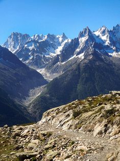 a man riding a bike on top of a rocky mountain side with snow covered mountains in the background