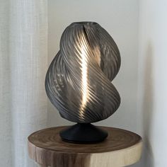 a black vase sitting on top of a wooden table next to a white wall and curtain