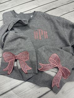 a gray sweatshirt with pink bows on the front and back, sitting on a wooden surface