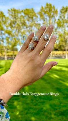 a woman's hand with two rings on it and some trees in the background