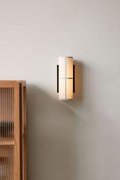 a wall light mounted on the side of a white wall next to a wooden cabinet