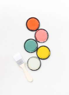 four different colors of paint sitting next to a brush on a white surface with one painted