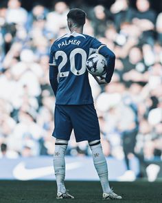 a soccer player is standing on the field with his ball in his hand and fans behind him