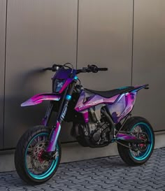 a pink and blue dirt bike parked next to a wall