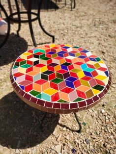 a multicolored mosaic table sitting on top of a dirt ground next to chairs