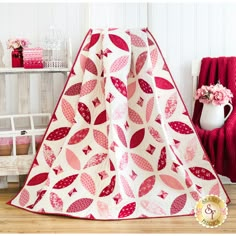 a red and white quilted blanket sitting on top of a wooden floor next to a chair