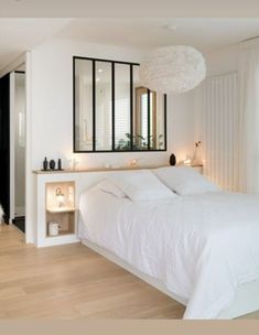 a white bed sitting in a bedroom next to a mirror and table with candles on it