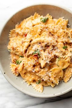 a white bowl filled with pasta and sauce on top of a marble countertop next to a wooden spoon