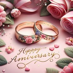 two gold wedding rings surrounded by pink roses and greenery with the words happy anniversary