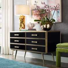 a black and gold dresser with flowers on top in a room next to a green chair