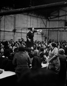 a woman standing on top of a wooden pole in front of a large group of people