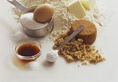 an assortment of ingredients including eggs, sugar and butter on a white surface with measuring spoons