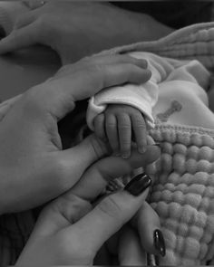 a woman holding a baby's hand while laying on top of a bed next to another person