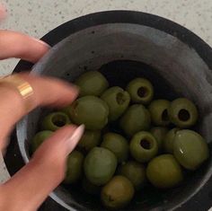 a woman's hand reaching for green olives in a bowl