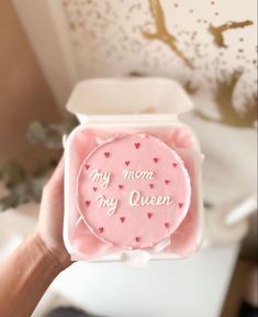 a person holding up a pink cake in a box with the words my mom, my queen written on it