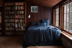 a bed sitting under a window in a bedroom next to a book shelf filled with books