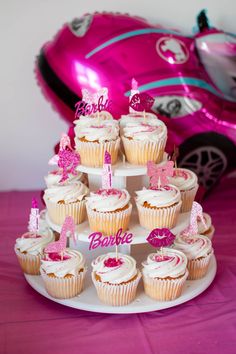 cupcakes are arranged on a cake stand in front of a pink car