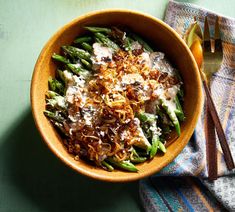 a wooden bowl filled with green beans covered in cheese and other toppings next to a fork