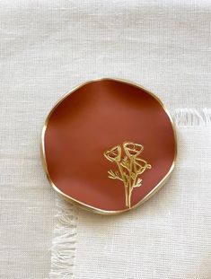 a red plate with gold flowers on it sitting on a white cloth covered tablecloth