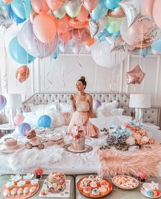 a woman sitting on top of a bed surrounded by balloons and desserts in front of her