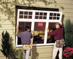 two men working on a window in front of a house