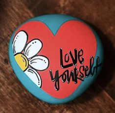 a painted rock that says love yourself with a heart and flower on the top, sitting on a wooden surface