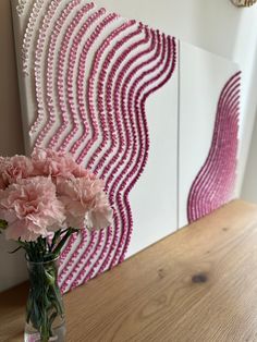 pink carnations are in a vase on a table next to a wall art piece