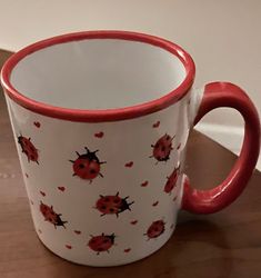 a red and white coffee cup with ladybugs on it sitting on a table