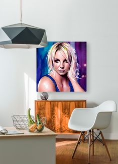 a painting of a blonde woman on a white wall above a wooden table and chair