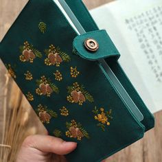 a person holding a green book with flowers on it and a button in the middle