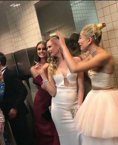 two women in white dresses are talking to each other while another woman is taking a selfie