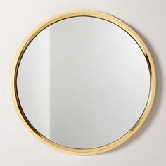 a round mirror hanging on the wall next to a white wall with a gold frame