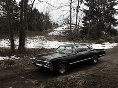 an old black car parked on the side of a dirt road in front of some trees