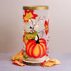 a glass vase with autumn leaves and pumpkins painted on the inside, sitting on a table