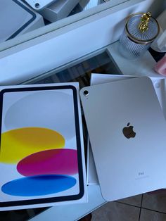 an apple ipad in its box next to another one on the table with other items