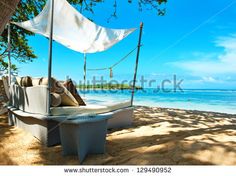 a couch sitting on top of a sandy beach next to the ocean under a canopy