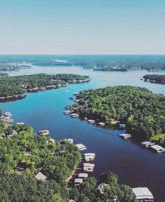 an aerial view of a lake surrounded by green trees and houses in the distance with blue sky