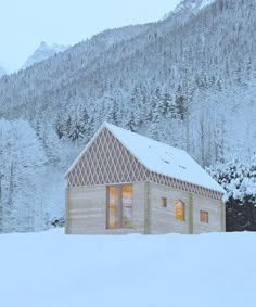 a small wooden cabin sitting in the middle of a snow covered field with mountains in the background