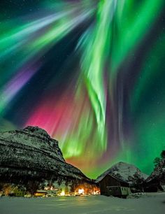 the aurora is in full color as it moves across the sky over some snow covered mountains