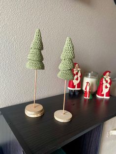 three small crocheted christmas trees sitting on top of a table next to candles