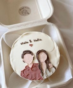 a cake with two people on it in a white box next to an empty container